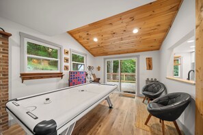 Mesa de bilhar em sala com piso de madeira, parede de tijolos e teto com vigas aparentes.