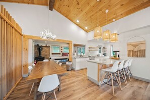 A modern kitchen with white cabinets, a wooden island, and a dining area with a wooden table and white chairs.