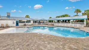 A swimming pool with lounge chairs, a covered seating area, and a building with a blue door. - Modern Beach Condo, Heated Pool Access (Tybee Island)