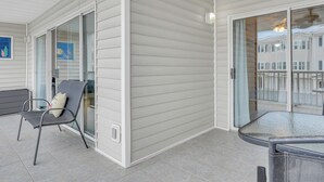 A covered outdoor area with a sliding glass door, a metal chair, and a small table. - Modern Beach Condo, Heated Pool Access (Tybee Island)