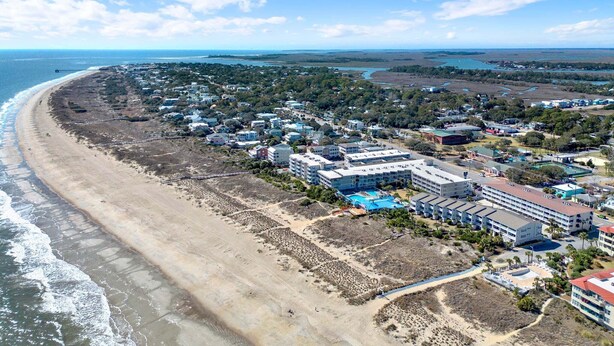 An aerial view of a coastal town with beachfront properties, a pier, and a hotel with multiple buildings and a swimming pool. - Modern Beach Condo, Heated Pool Access (Tybee Island)