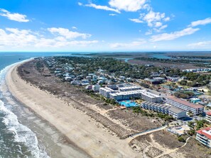 Une vue aérienne d’une ville côtière, avec des propriétés situées en bord de mer, une jetée et un hôtel composé de plusieurs bâtiments et doté d’une piscine.