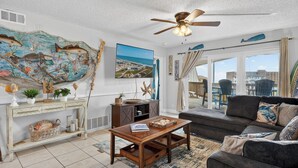 A living room with a large fish mural, a ceiling fan, a sofa, and a view through large windows.