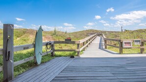A wooden boardwalk leading to a beach with a surfboard and a sign prohibiting carts beyond a certain point.
