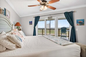 A bedroom with a bed, a ceiling fan, a window with curtains, and a view of the outside.