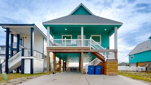 Una casa sulla spiaggia su due piani, con un balcone, un portico coperto e una scala che conduce al piano superiore.