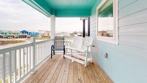 Un portico coperto con due poltrone Adirondack, un patio in legno e vista su altri edifici sullo sfondo.