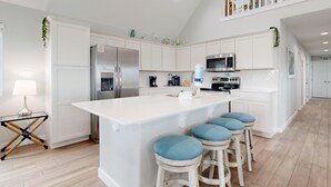 Una cucina moderna con mobili bianchi, elettrodomestici in acciaio inossidabile e un'isola centrale con sgabelli da bar.