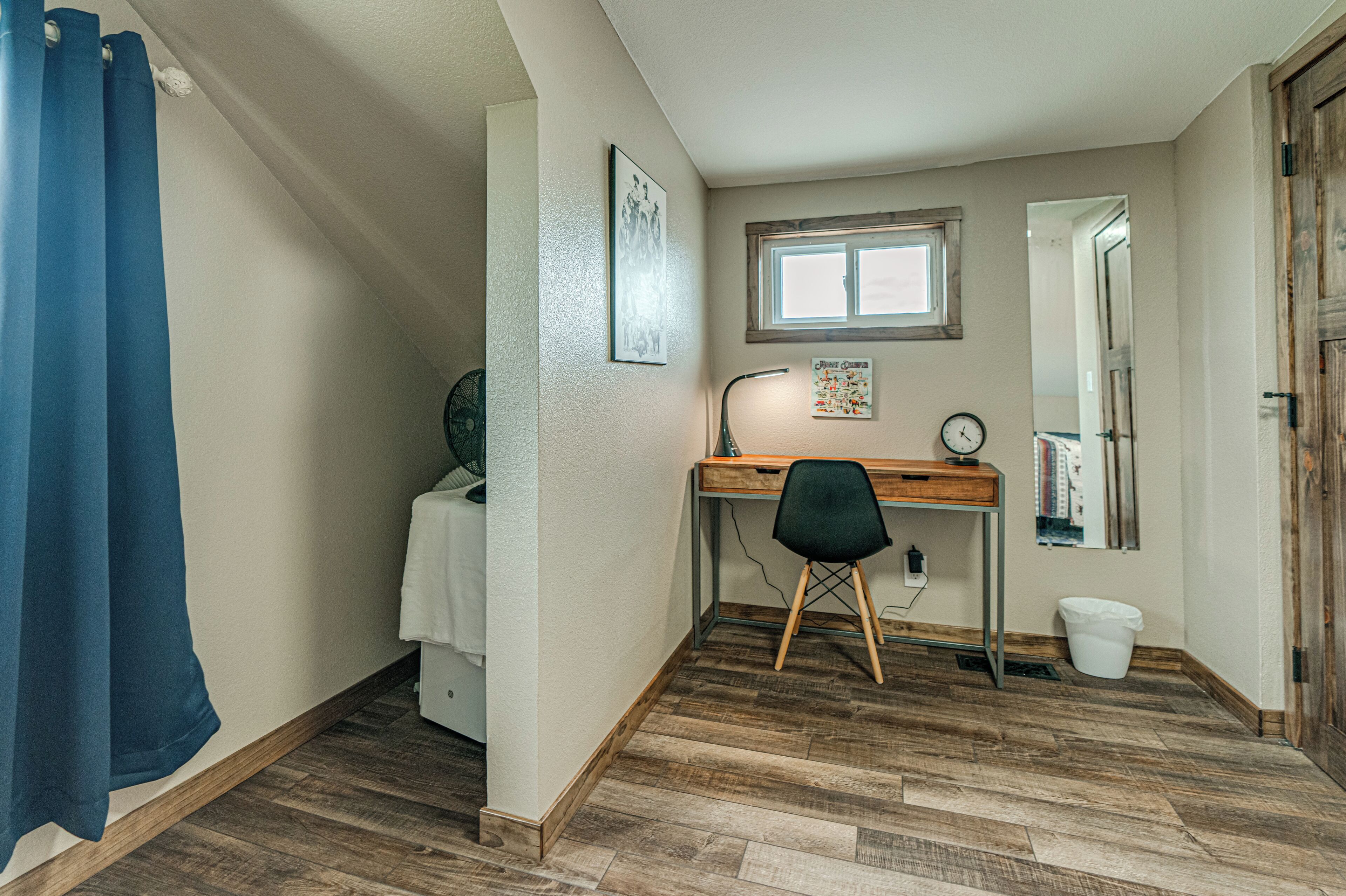 A room with a wooden desk, a chair, a bed, a window, and a door.