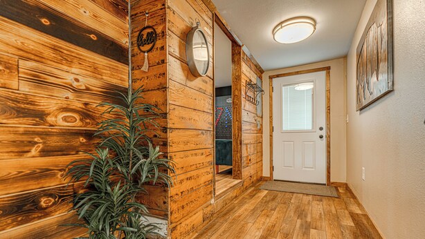 A hallway with wooden walls, a potted plant, a door, and a light fixture. - Country Living with Modern Amenities and Hot Tub (Bismarck)