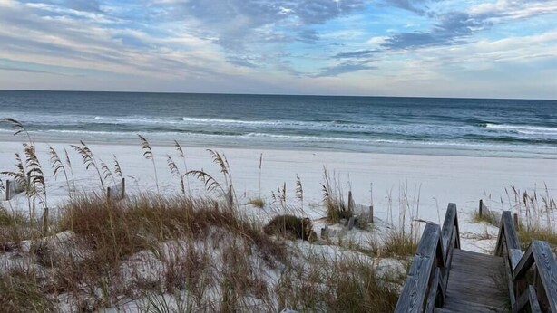 A beach with a wooden boardwalk leading to the water, surrounded by sand and sparse vegetation. - Sea 'n Stars Cape San Blas Vacation Rental (Port St. Joe)