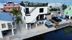 A modern multi-story house with a rooftop deck, a swimming pool, and a dock extending into the water.
