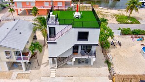 A modern two-story building with a rooftop deck, a pool, and a beach area with lounge chairs.