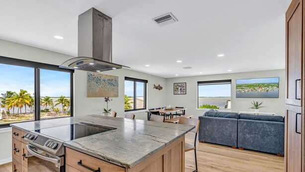 A modern kitchen with a large island, wooden cabinets, and a view of the beach.