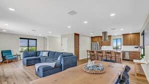 A modern living room with a sectional sofa, dining table, and kitchen area with wooden cabinets and stainless steel appliances.