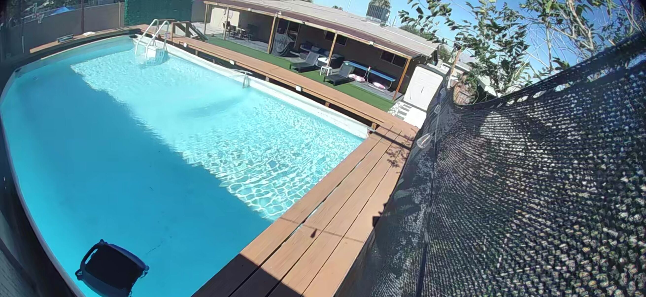 Una piscina con terraza de madera, un área de descanso con asientos y una sección cubierta con vista a la piscina.