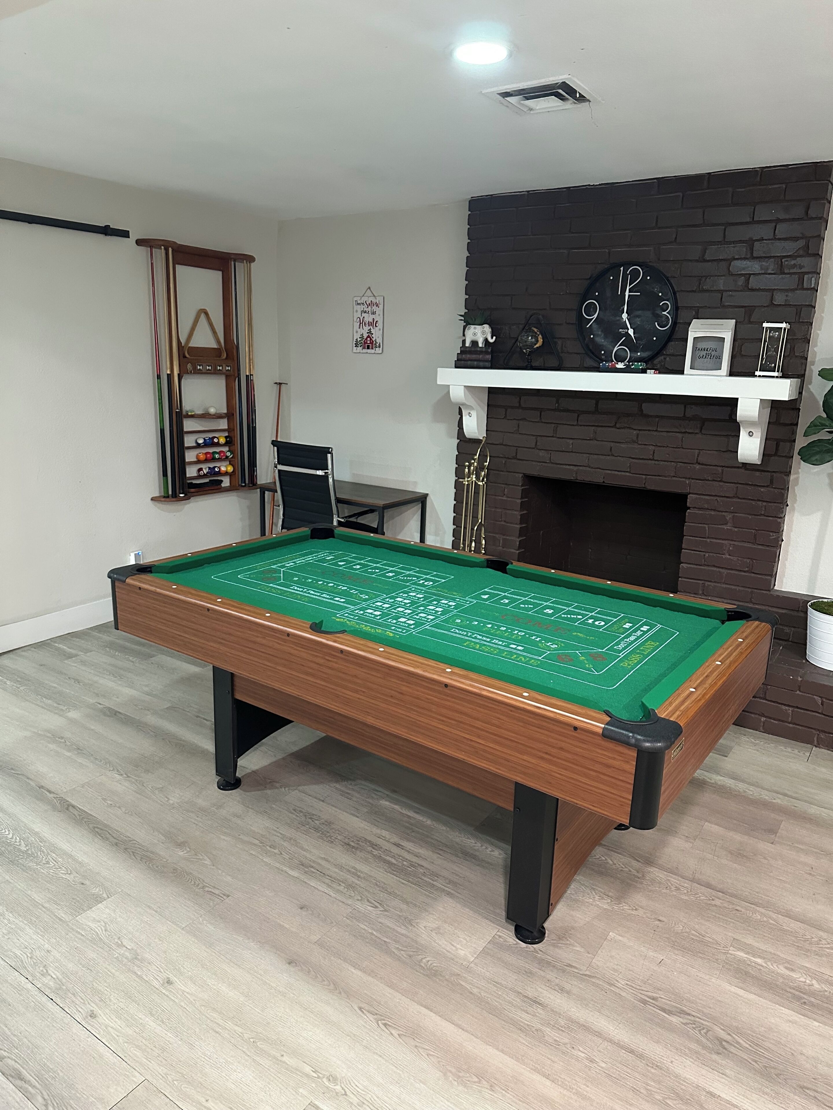 Une table de billard dans une pièce dotée d’une cheminée en briques, d’une horloge et d’une étagère ornée d’objets décoratifs.