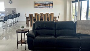 A modern living room with a black leather sofa, a dining area with wooden chairs and a table, and a large window with a view of a pier. - Sleeps 14 - 3 minute walk to beach, 5 minute drive to "The Dunes" Golf Course  (Moonta Bay)