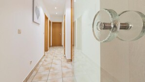 Un couloir doté d’un sol carrelé, de portes en bois et d’une poignée de porte en verre.