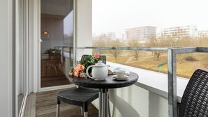 Un balcon avec une table préparée pour le thé, une chaise et une vue sur les bâtiments au loin.