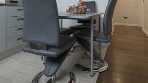 A modern kitchen with grey cabinets, a dining table with two chairs, and a small floral centerpiece.