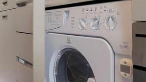 A modern laundry room with a front-loading washing machine, a shelf above the machine, and a control panel with various settings.
