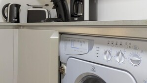 A compact kitchen with a washing machine, a coffee maker, and a toaster on the countertop.