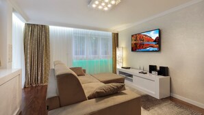 A modern living room with a sectional sofa, a flat-screen TV mounted on the wall, and a white entertainment unit.