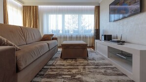 A modern living room with a beige sofa, a glass coffee table, and a flat-screen TV mounted on the wall.