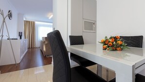 A modern dining area with a white table and black chairs, a bouquet of orange flowers, and a kitchen with a microwave.