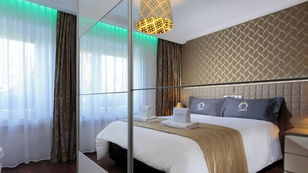 A modern hotel room with a large bed, a bedside table, a mirror, and a patterned wall.