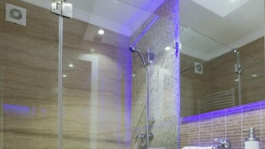 Un baño moderno con cabina de ducha de vidrio, pared de mármol y tocador negro con espejo.