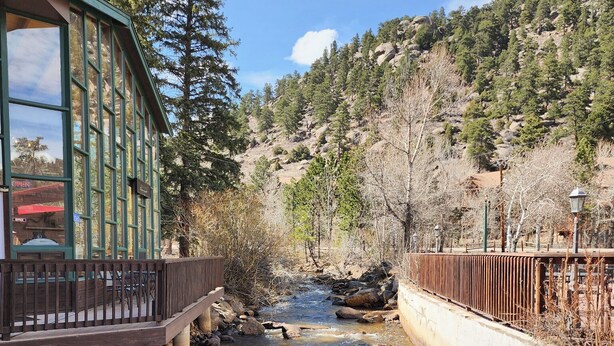 A bridge over a clear stream with a building on the left. - pacious Upper-Level Hotel Queen and Full-size beds with Views 208-210 (Estes Park)