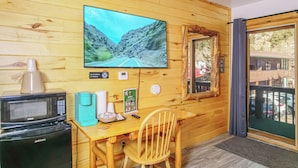 A wooden interior with a TV displaying a scenic road, a microwave, a coffee maker, a chair, and a window with a view. - pacious Upper-Level Hotel Queen and Full-size beds with Views 208-210 (Estes Park)