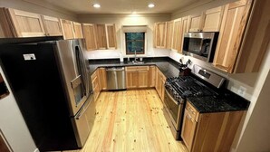 Una cocina con armarios de madera, electrodomésticos de acero inoxidable, un refrigerador negro, una estufa y un microondas.