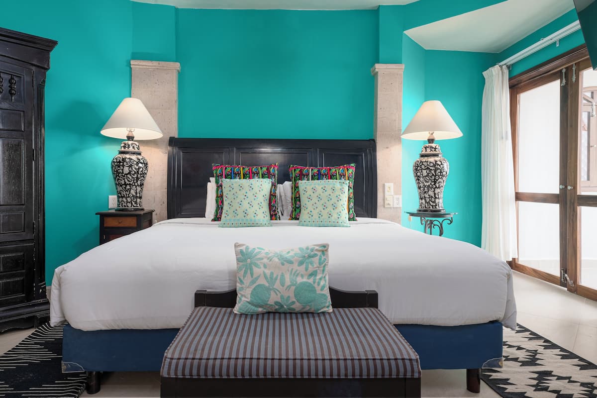A bedroom with a large bed, two bedside tables, a bench, and a window with curtains.