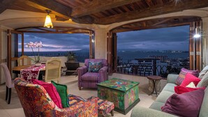A cozy interior with a wooden ceiling, a dining area, a sofa set, and a view of the city and sea. - Marcela Resort & Spa (Puerto Vallarta)