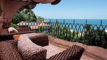 Ein Balkon mit Korbmöbeln, Blick auf das Meer und einem Metallgeländer.