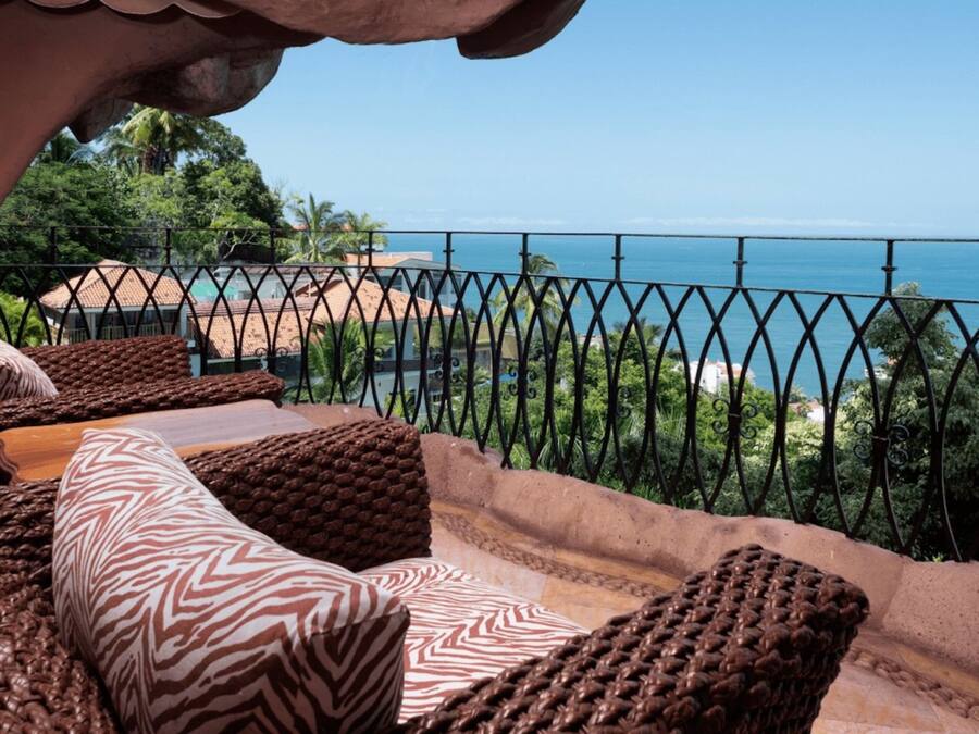 Ein Balkon mit Korbmöbeln, Blick auf das Meer und einem Metallgeländer.