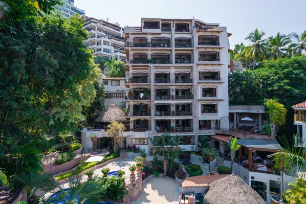 Un hotel de varios pisos con balcones, una zona de piscina y abundante vegetación.
