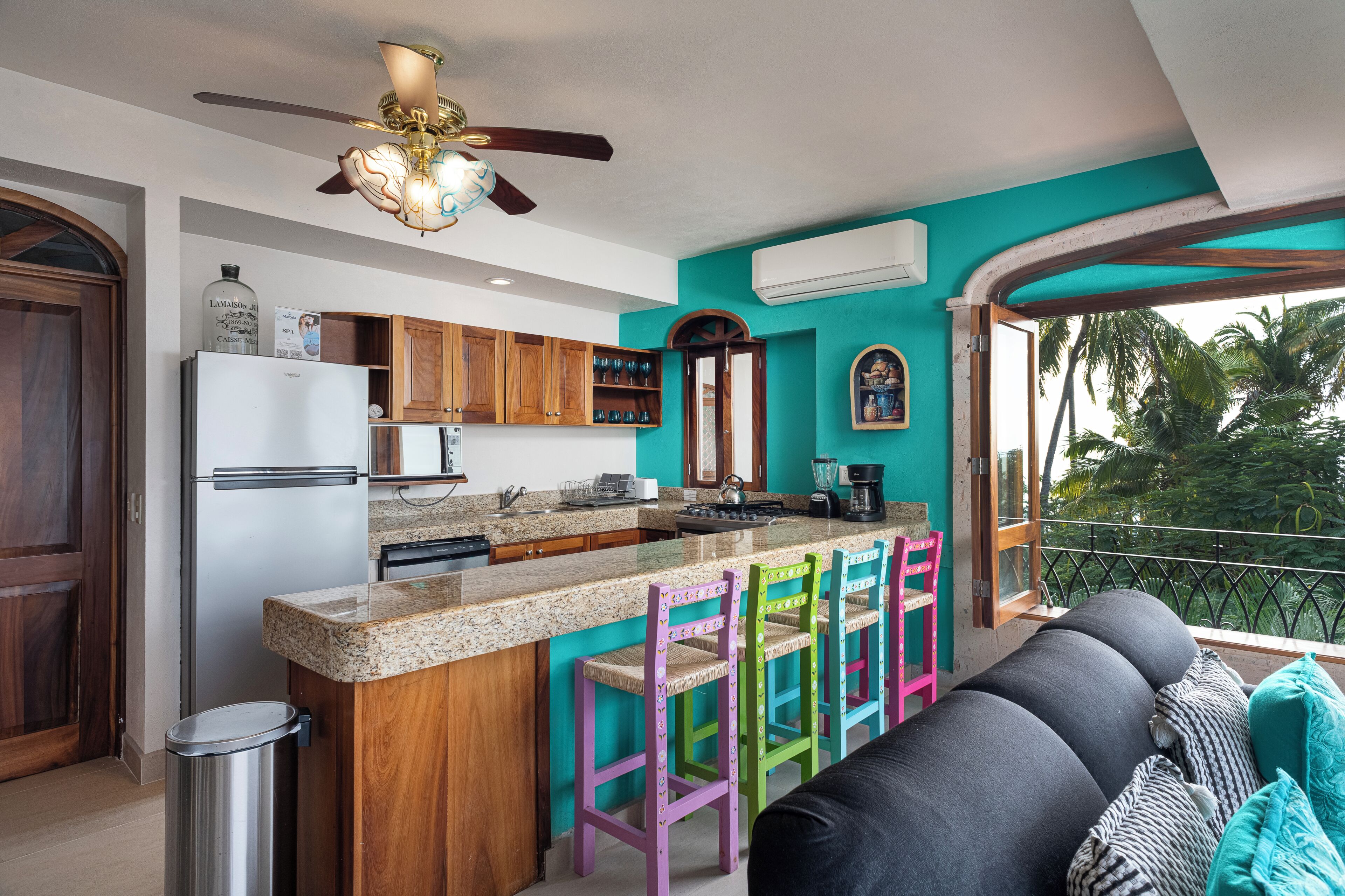 A kitchen with a central island, wooden cabinets, a refrigerator, and colorful bar stools.
