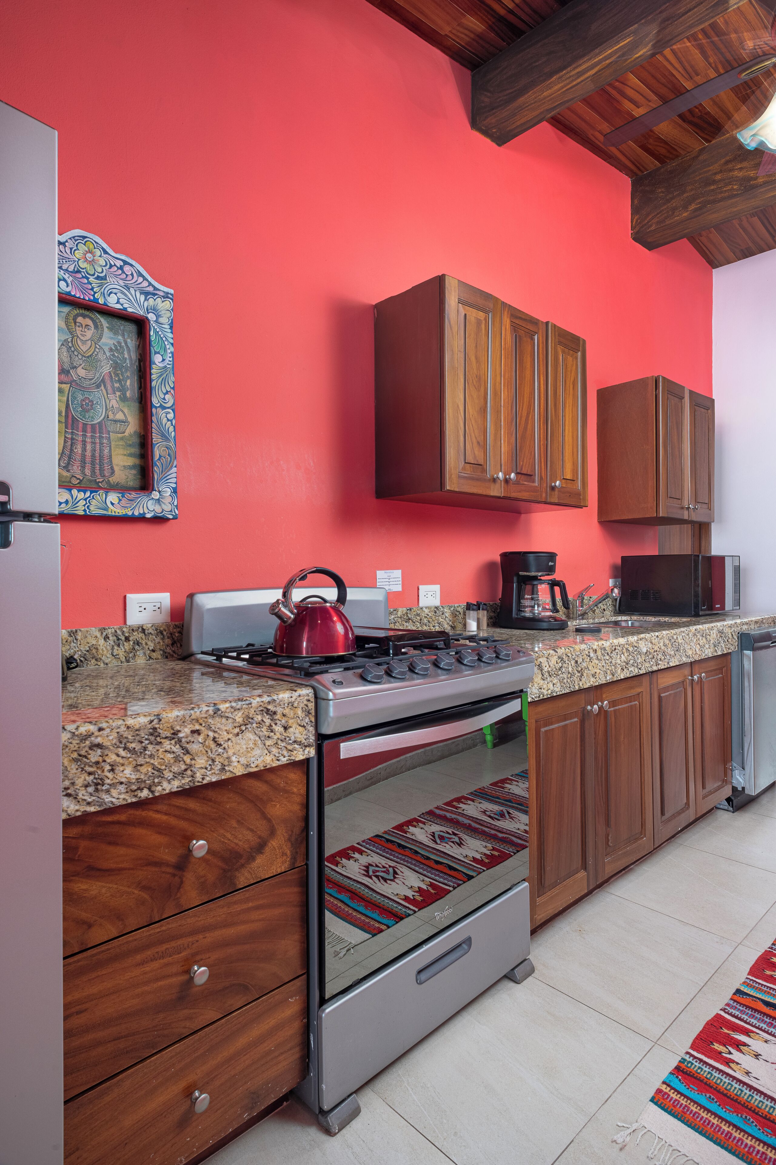 Una cocina con armarios de madera, una pared roja, una estufa y un microondas.