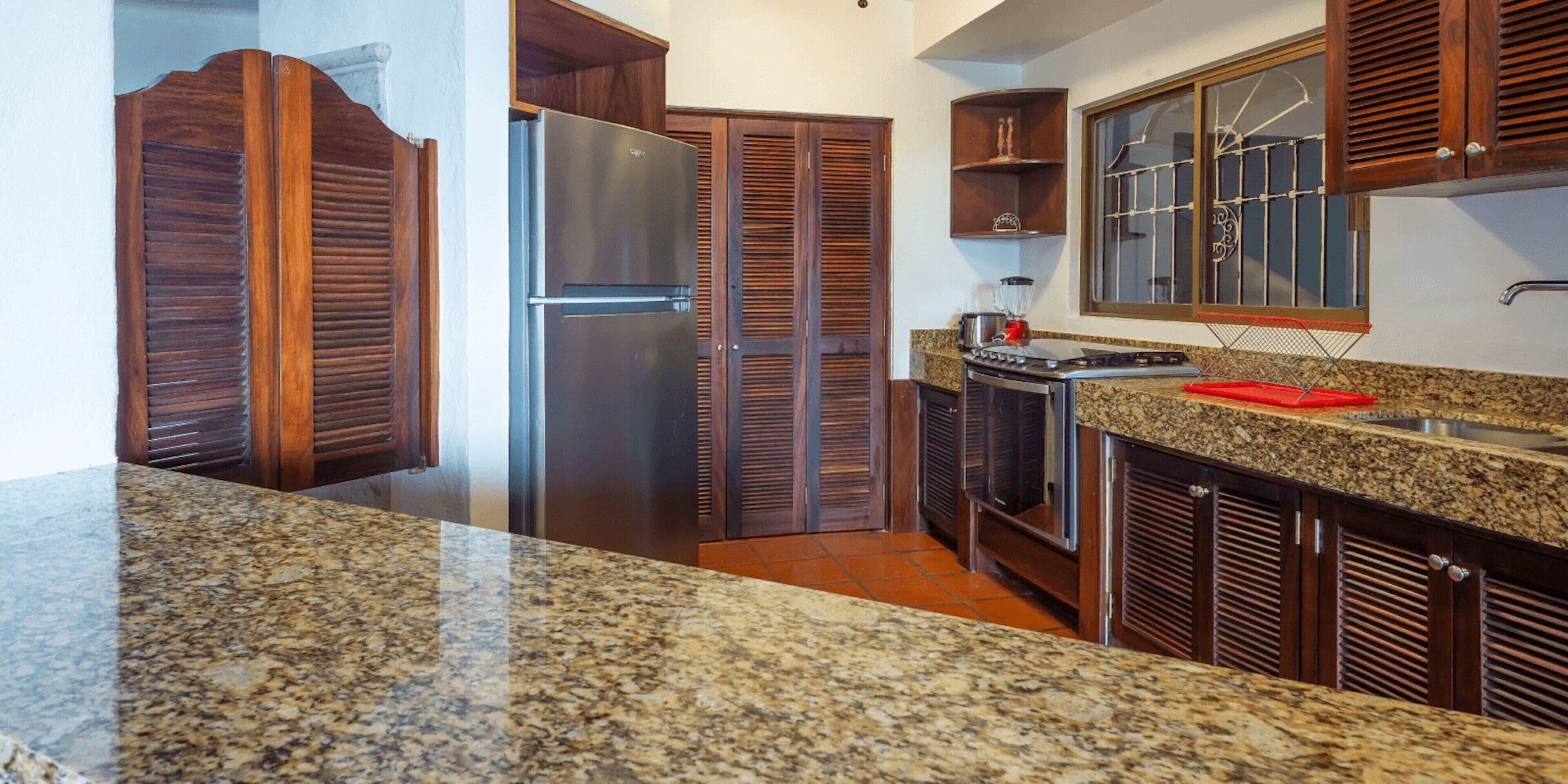 A kitchen with granite countertops, a stainless steel refrigerator, wooden cabinets, and a built-in oven.