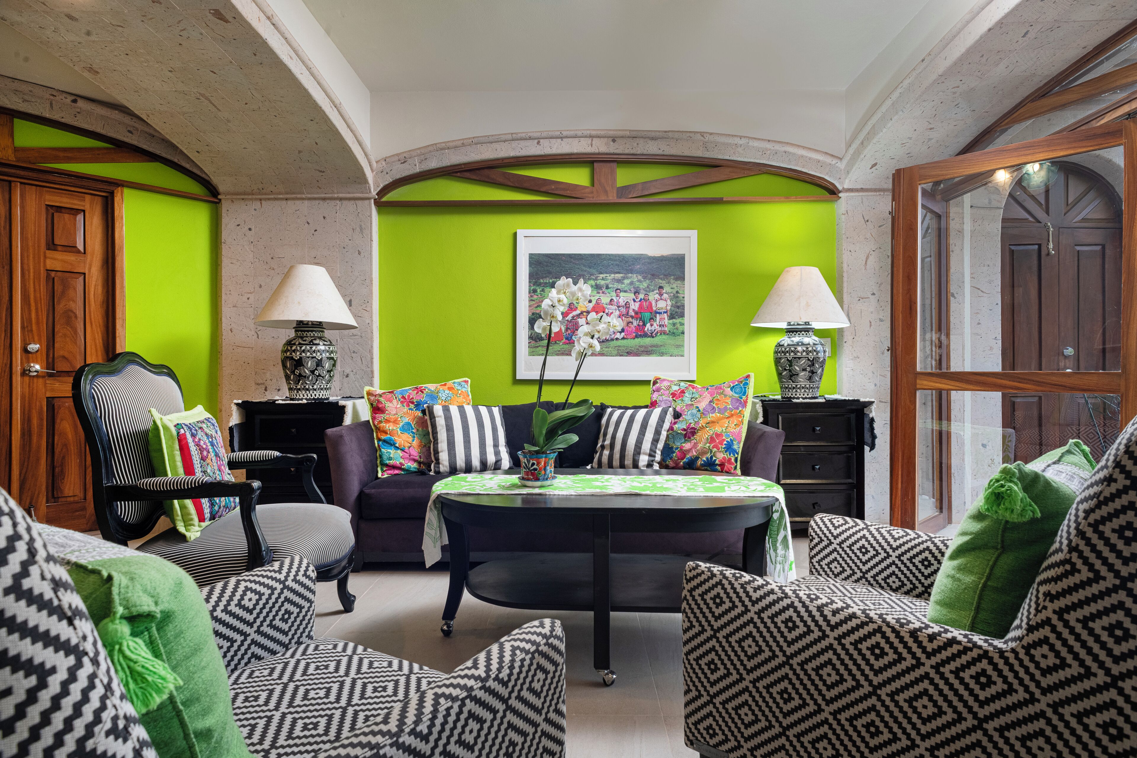 Un soggiorno con una parete verde, un divano nero, cuscini decorati, un tavolino da caffè e due lampade.