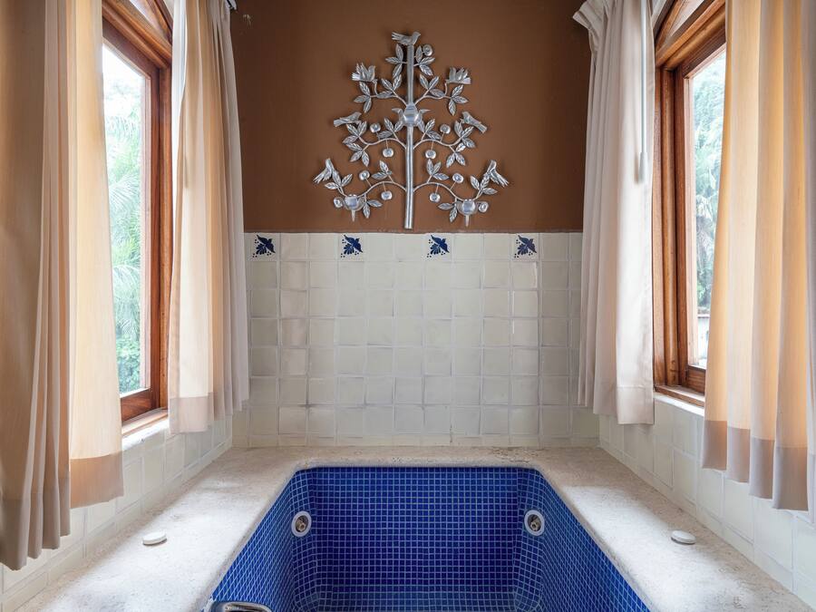Une salle de bain avec une baignoire carrelée de carreaux bleus, des rideaux beiges et un élément décoratif mural.