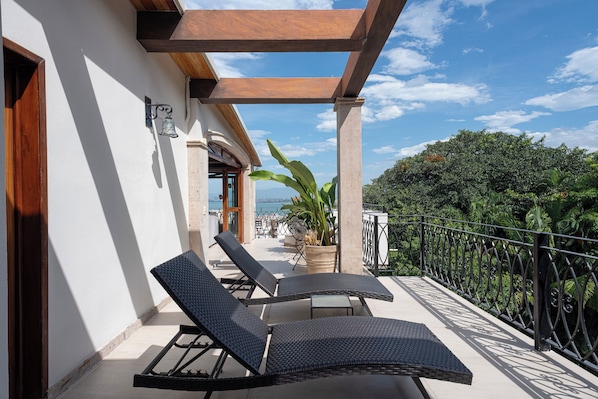 A balcony with two lounge chairs, a potted plant, and a view of the sea.