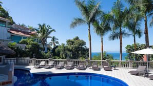 A pool area with lounge chairs, palm trees, and a view of the ocean. - Marcela Resort & Spa (Puerto Vallarta)