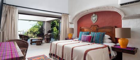 A bedroom with a bed, a nightstand, a chair, a table, and a view of greenery outside.