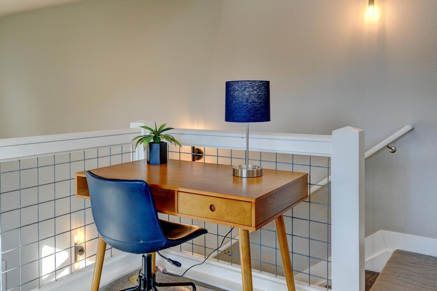 Un petit espace de travail comprenant un bureau en bois, une chaise bleue, une lampe et une plante en pot.
