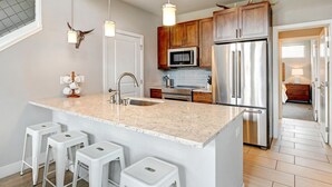 Una cocina moderna con una isla central, electrodomésticos de acero inoxidable, armarios de madera e iluminación colgante.